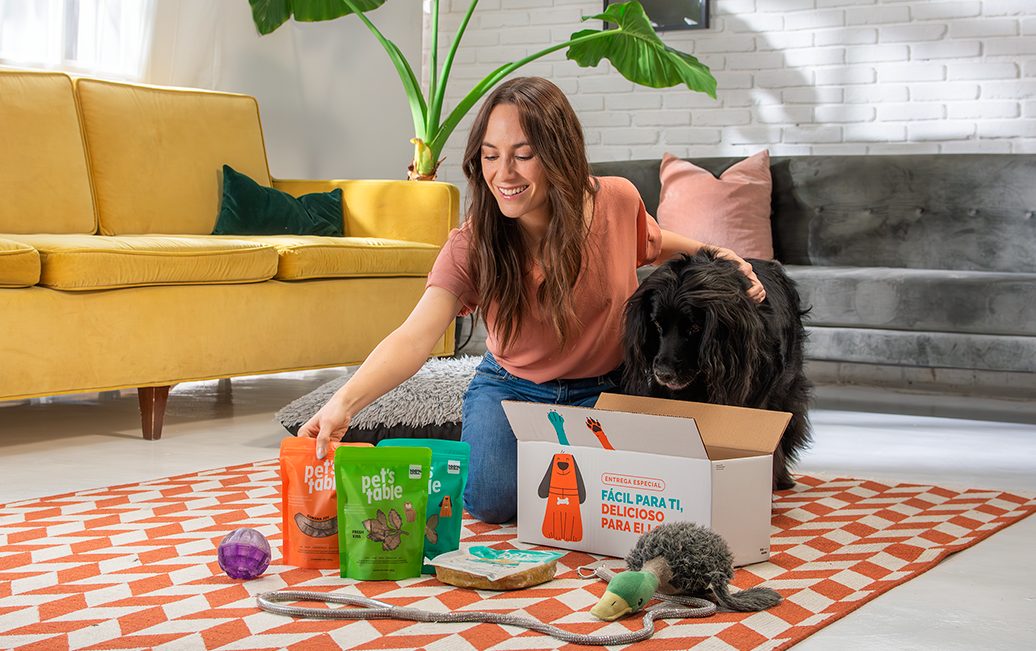Mujer abriendo una caja de Pet's Table junto a su perro